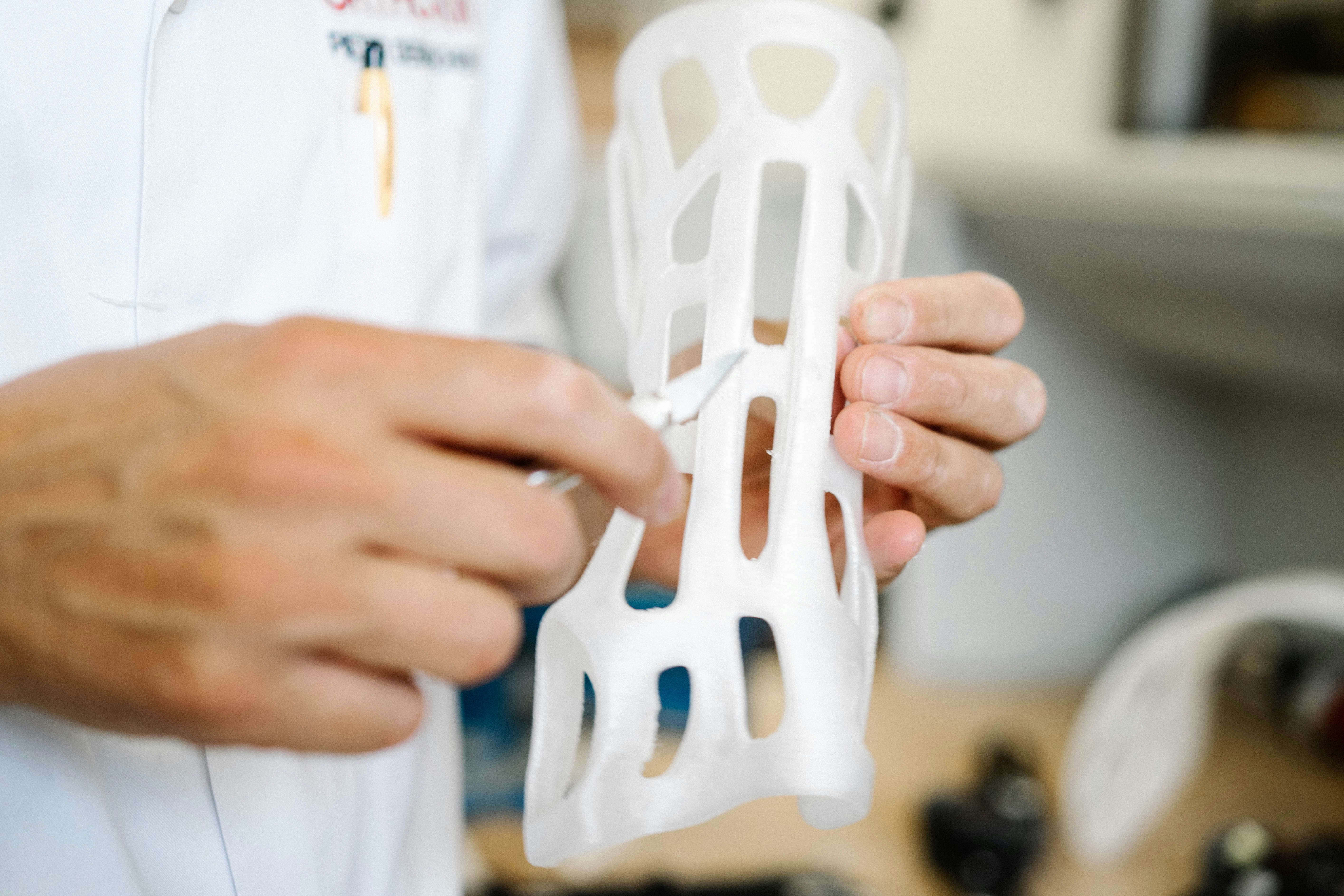Hands holding a white 3D printed orthotic brace in a workshop setting